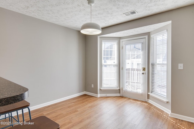 unfurnished dining area featuring light wood-style flooring, baseboards, visible vents, and a textured ceiling