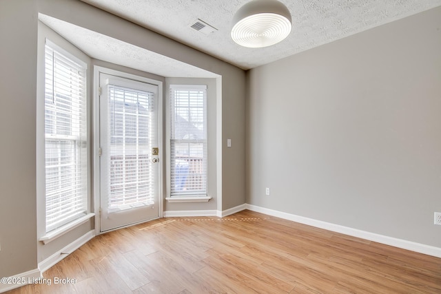 unfurnished room with a wealth of natural light, visible vents, light wood-type flooring, and baseboards