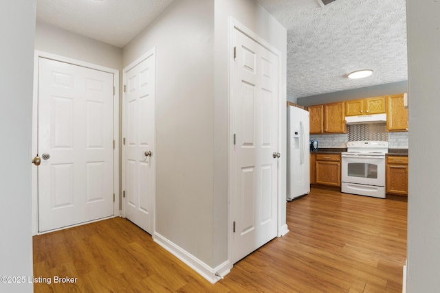 hallway featuring light wood-type flooring, baseboards, and a textured ceiling