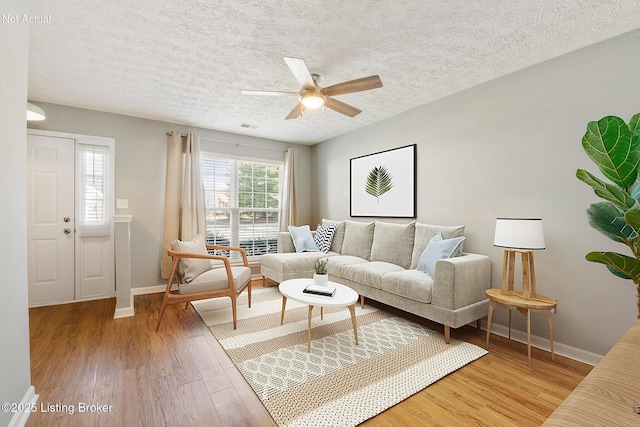 living area featuring a ceiling fan, visible vents, wood finished floors, baseboards, and a textured ceiling