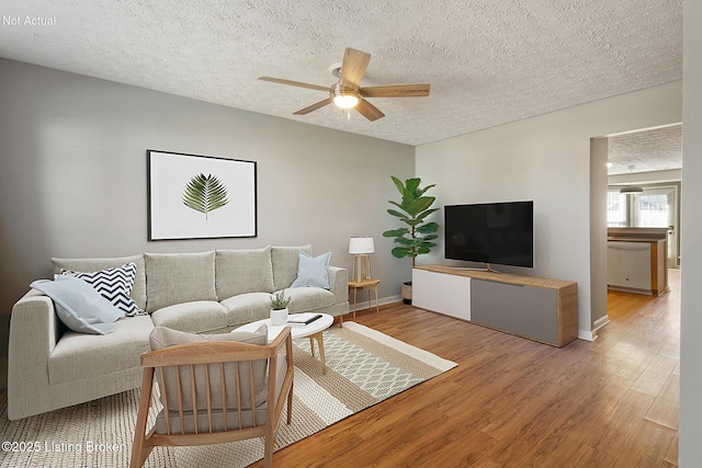 living area featuring a textured ceiling, wood finished floors, baseboards, and ceiling fan