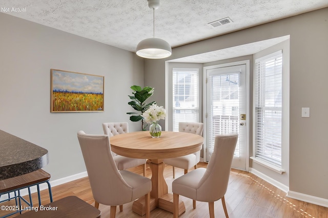 dining room with light wood-style flooring, baseboards, visible vents, and a textured ceiling