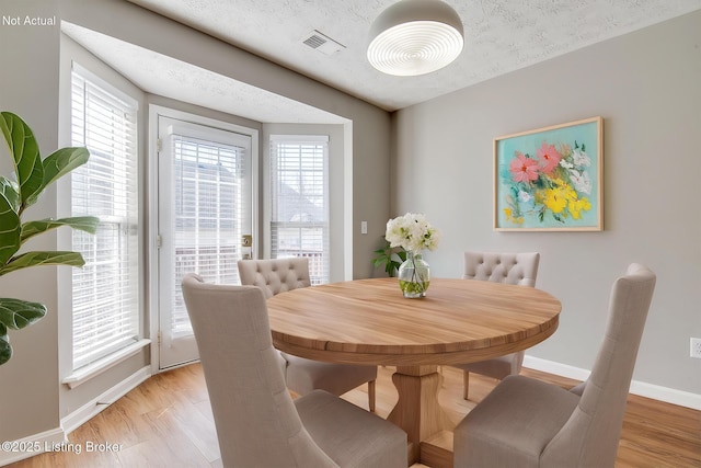 dining room with visible vents, light wood-style flooring, a textured ceiling, and baseboards