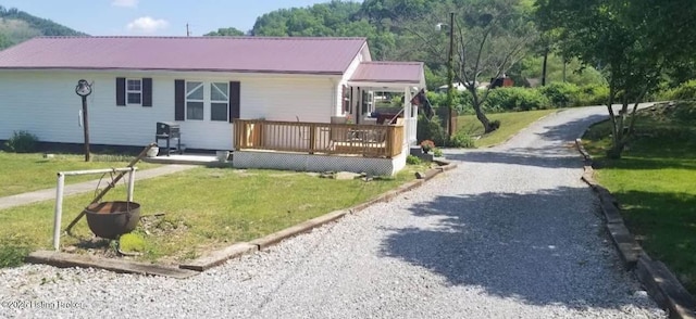 view of front of home with a front yard, metal roof, driveway, and a wooden deck