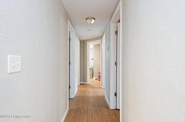 hall featuring baseboards, wood finished floors, and a textured wall