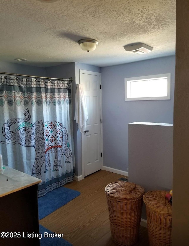 bathroom with a shower with curtain, wood finished floors, baseboards, and a textured ceiling