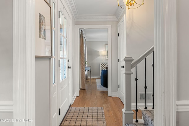 hallway featuring baseboards, visible vents, light wood finished floors, ornamental molding, and stairs