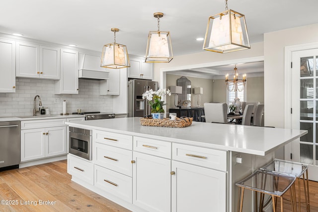 kitchen with a sink, ornamental molding, light countertops, stainless steel appliances, and light wood-type flooring