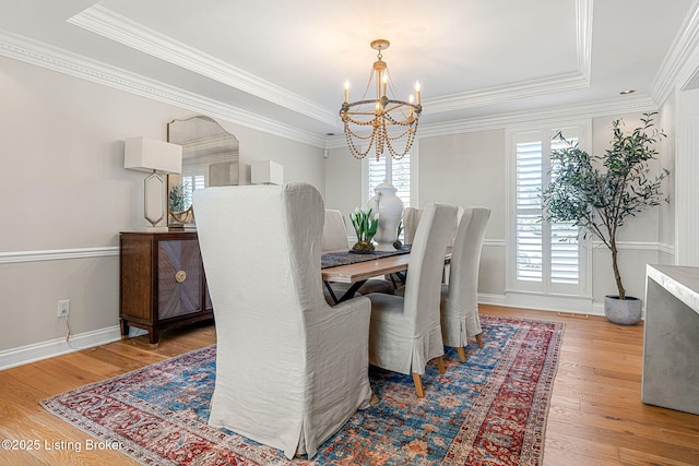 dining room featuring a tray ceiling, wood-type flooring, an inviting chandelier, crown molding, and baseboards