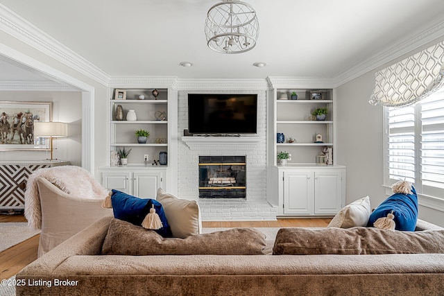 living room featuring built in shelves, wood finished floors, a fireplace, and crown molding