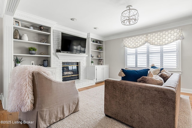 living room featuring built in shelves, wood finished floors, a brick fireplace, and ornamental molding