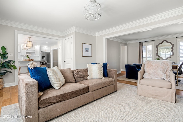 living area featuring crown molding, a notable chandelier, light wood-style floors, and baseboards