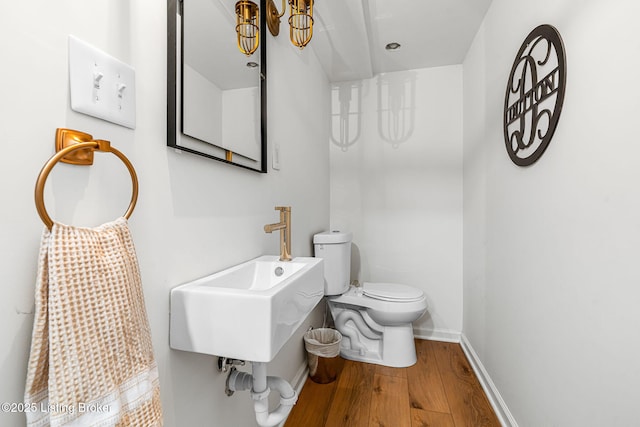 bathroom with toilet, wood finished floors, baseboards, and a sink