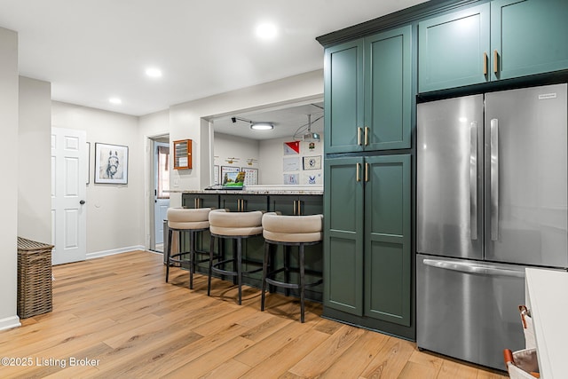 kitchen featuring baseboards, light wood-style floors, green cabinets, and freestanding refrigerator