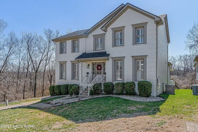 view of front of house with a front yard, central AC unit, and brick siding