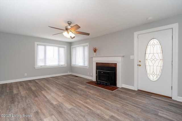 unfurnished living room with a ceiling fan, a wood stove, wood finished floors, and baseboards