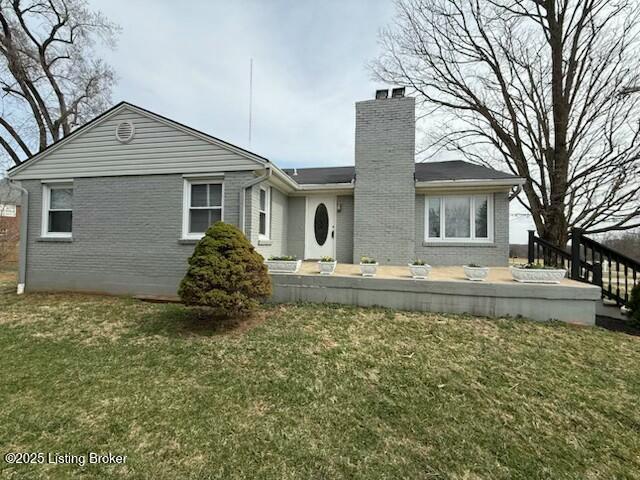 back of house with a yard, brick siding, and a chimney