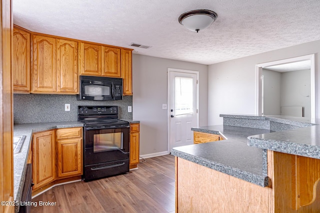 kitchen featuring visible vents, black appliances, wood finished floors, decorative backsplash, and baseboards