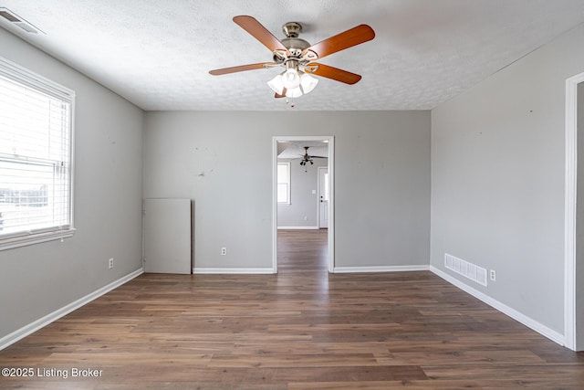 empty room featuring visible vents, a textured ceiling, wood finished floors, and a ceiling fan