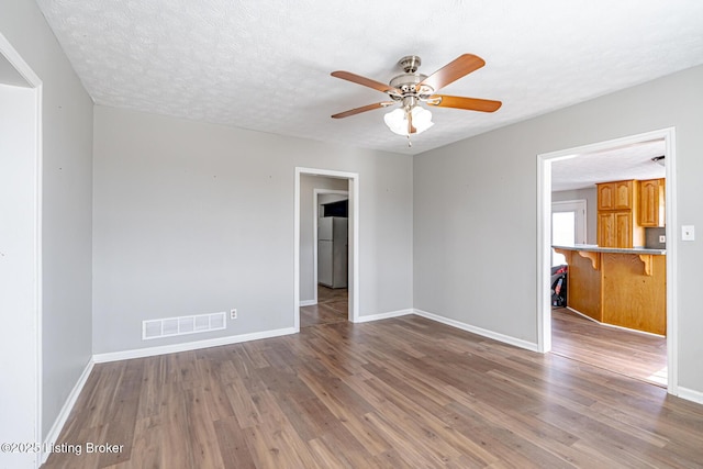 unfurnished room featuring a textured ceiling, wood finished floors, visible vents, and ceiling fan