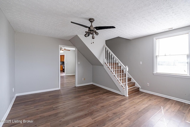 unfurnished living room with wood finished floors, a ceiling fan, visible vents, baseboards, and stairs