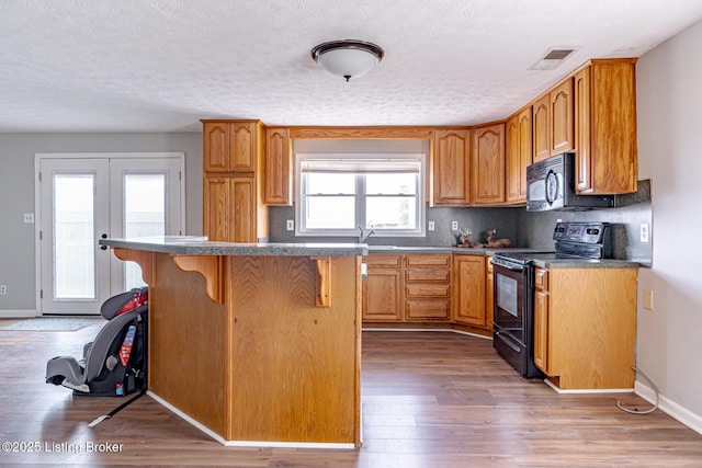 kitchen featuring a breakfast bar area, wood finished floors, visible vents, decorative backsplash, and black appliances