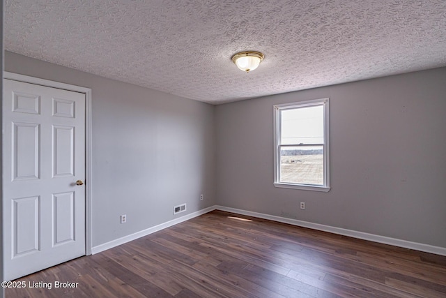 unfurnished room with visible vents, baseboards, dark wood-type flooring, and a textured ceiling