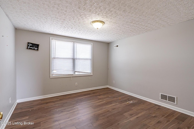 spare room with a textured ceiling, wood finished floors, visible vents, and baseboards