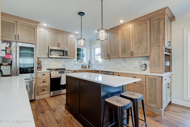 kitchen featuring a sink, wood finished floors, a center island, appliances with stainless steel finishes, and light countertops