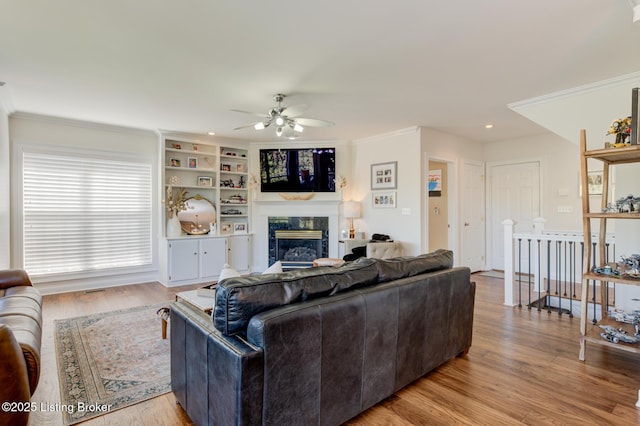 living room with light wood-type flooring, a high end fireplace, recessed lighting, crown molding, and ceiling fan