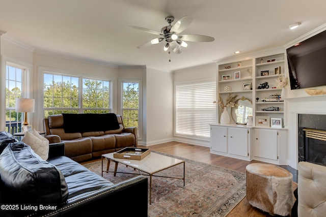 living area featuring wood finished floors, baseboards, a premium fireplace, ceiling fan, and crown molding