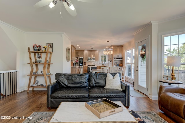 living room featuring dark wood-type flooring, ceiling fan with notable chandelier, baseboards, and ornamental molding