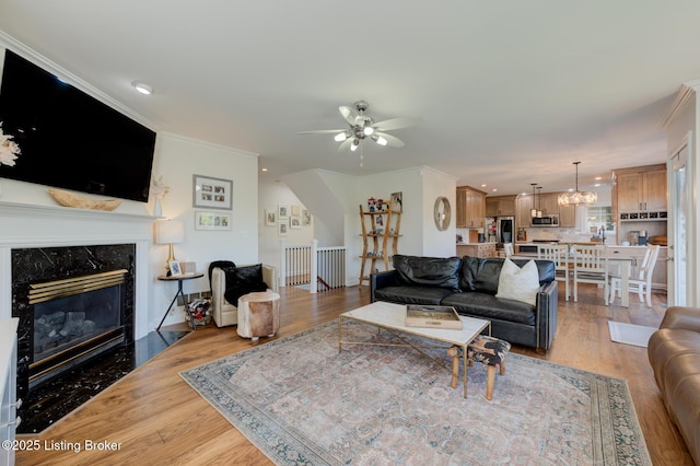 living area with ceiling fan with notable chandelier, a fireplace, light wood-type flooring, and crown molding