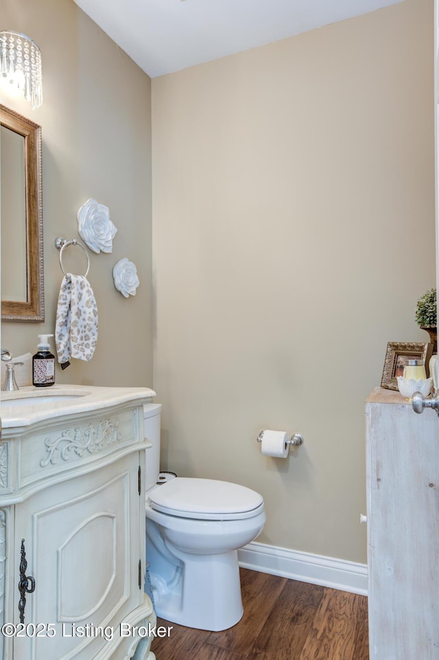 half bath featuring baseboards, toilet, wood finished floors, and vanity