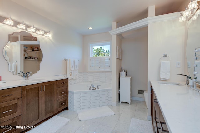 bathroom with visible vents, two vanities, a garden tub, and a sink