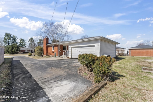 exterior space featuring an attached garage, a chimney, a front lawn, aphalt driveway, and brick siding