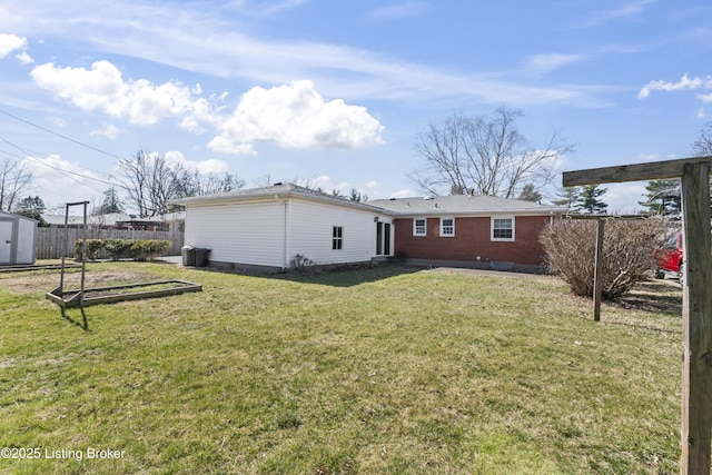 rear view of house with a storage unit, an outbuilding, fence, a yard, and brick siding