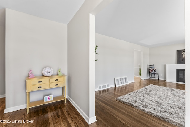 interior space with a fireplace with flush hearth, wood finished floors, visible vents, and baseboards