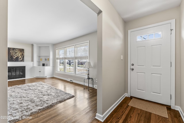 foyer entrance featuring a glass covered fireplace, visible vents, wood finished floors, and baseboards