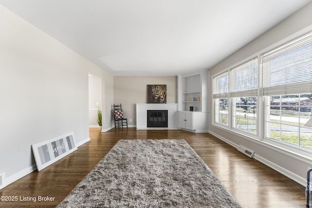 living area featuring visible vents, baseboards, dark wood-type flooring, and a glass covered fireplace