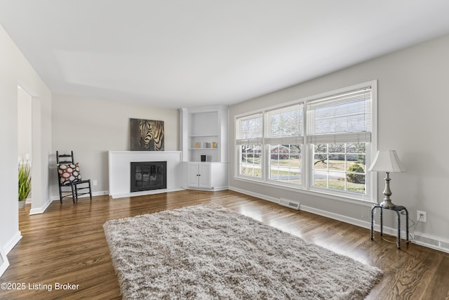 living room featuring visible vents, built in shelves, a glass covered fireplace, dark wood finished floors, and baseboards