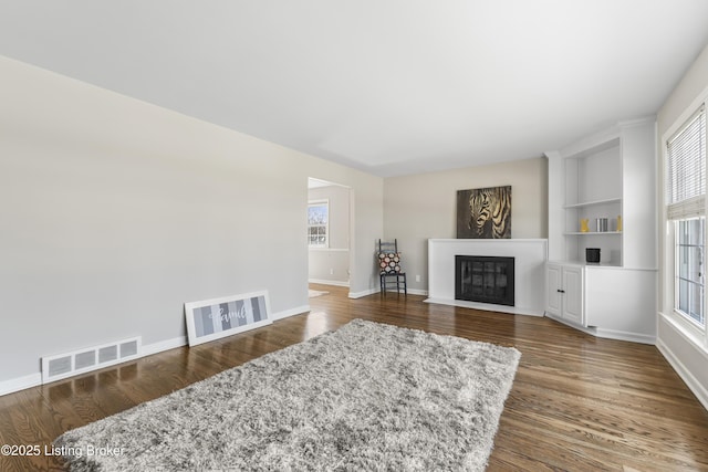 living area with visible vents, a fireplace with flush hearth, built in features, wood finished floors, and baseboards