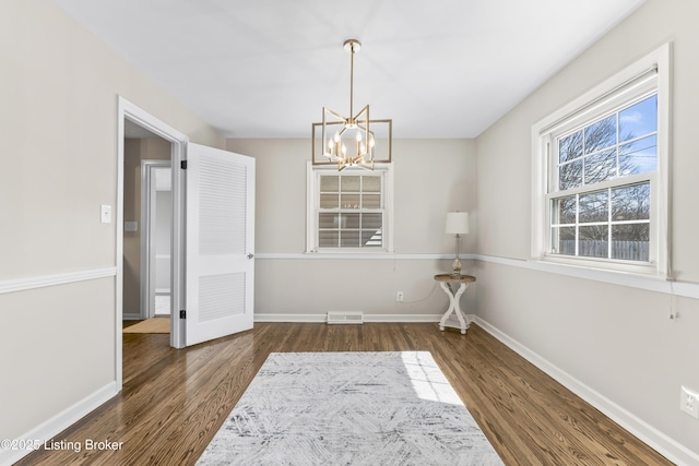 unfurnished dining area featuring a chandelier, visible vents, baseboards, and wood finished floors