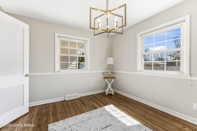 empty room with a notable chandelier, visible vents, baseboards, and wood finished floors