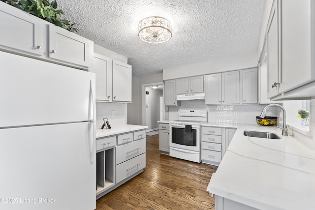 kitchen featuring a sink, under cabinet range hood, light stone counters, white appliances, and dark wood-style flooring