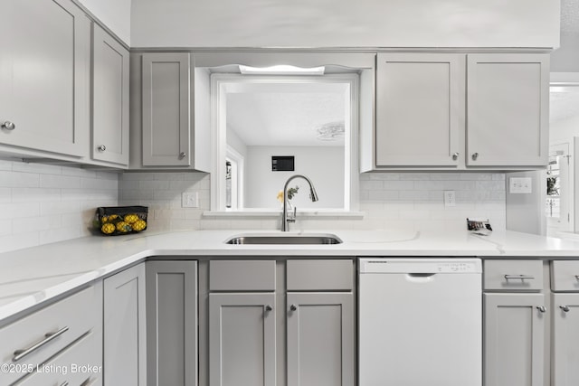 kitchen with tasteful backsplash, gray cabinets, white dishwasher, and a sink