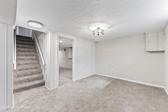 finished basement featuring stairway, a textured ceiling, baseboards, and carpet