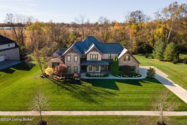 view of front of home with a forest view, a front lawn, metal roof, stone siding, and a standing seam roof