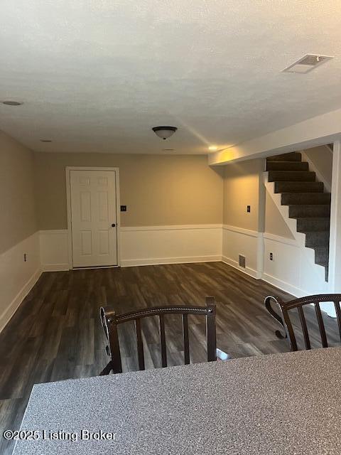 finished basement featuring visible vents, a wainscoted wall, a textured ceiling, wood finished floors, and stairway