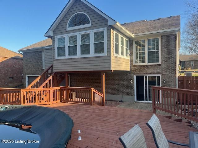 back of property with a wooden deck, brick siding, and fence